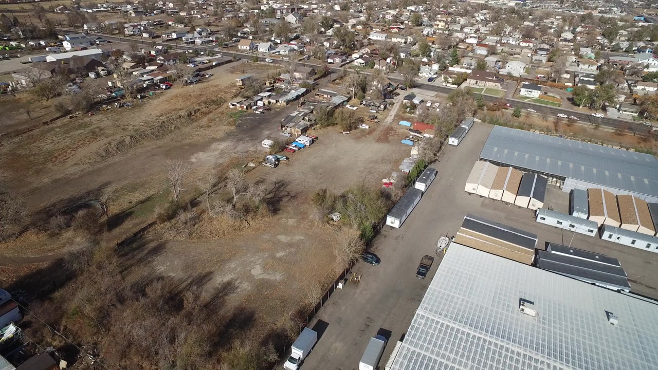 Aerial view of warehouse roofs, open dirt ground, trees, and nearby houses.
