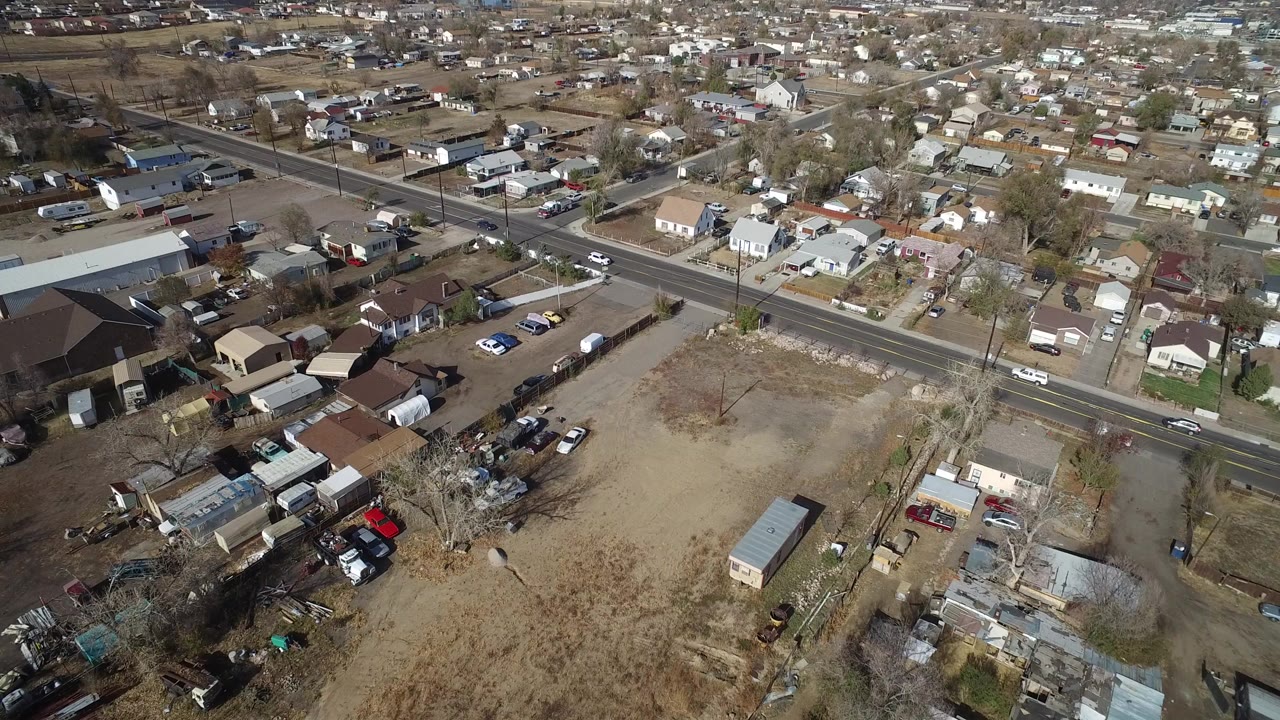Aerial view over homes, yards, a road, and parked cars