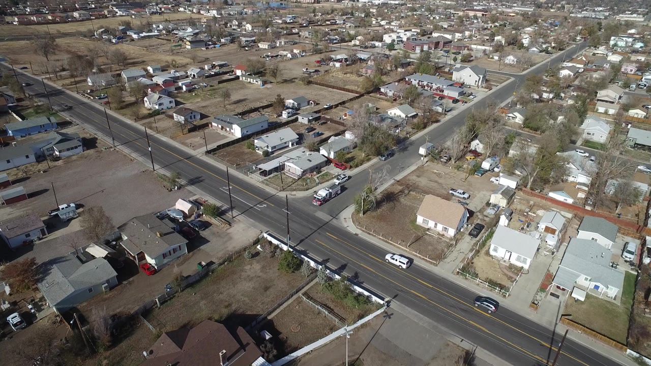 Oblique drone view in Westminster, Colorado, with cars moving along the main road, small houses and yards below, and no visible people in the frame.