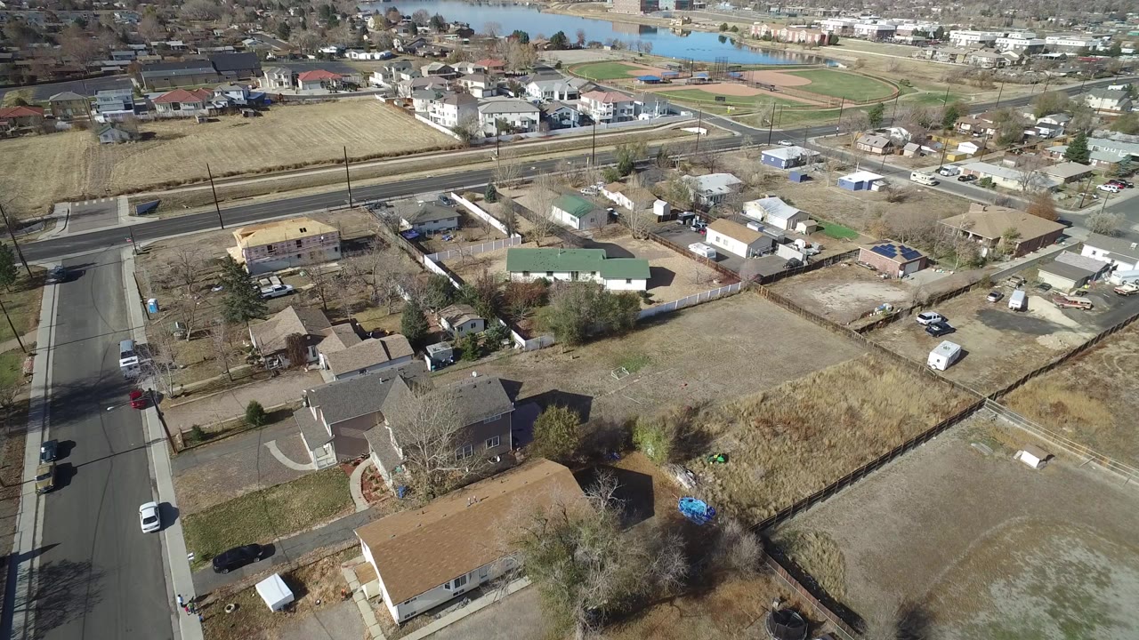 Aerial view of suburban homes, yards, roads, fields, and distant water.
