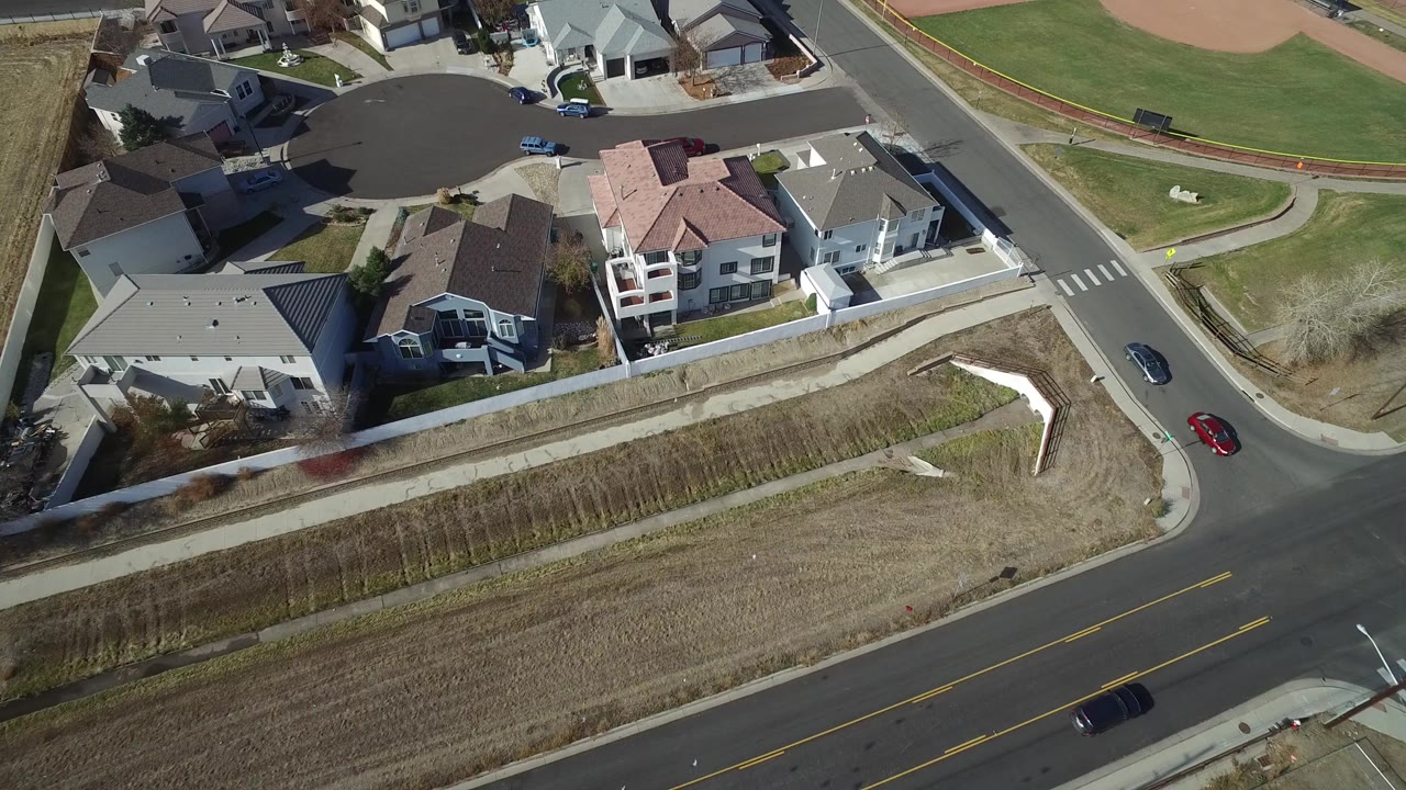 Aerial view of suburban homes beside a curved road and open ground.