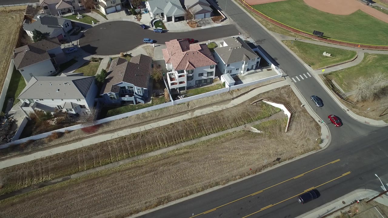 Aerial view in Westminster, Colorado showing rooftops, a cul-de-sac, bordering streets, a green ballfield edge, cars, and no visible people.