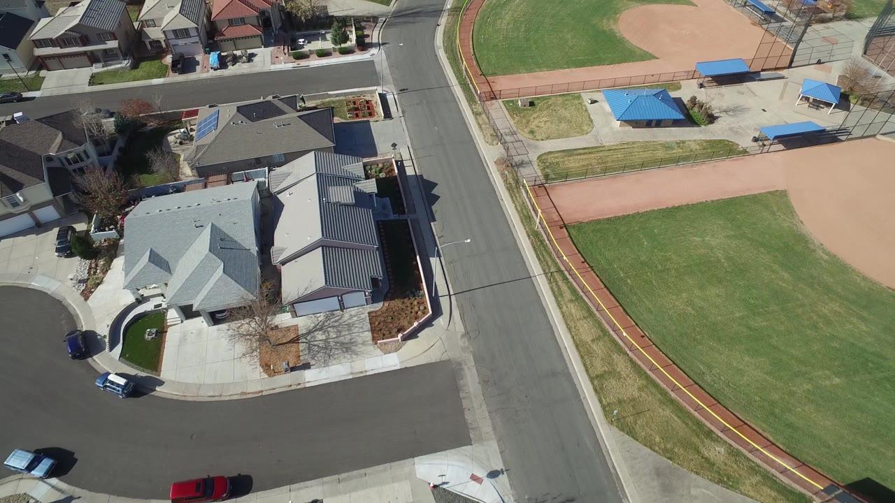 Overhead view of suburban homes beside a baseball field and curved street.