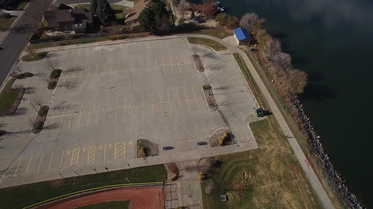 Aerial view of an empty parking lot beside green water and homes.