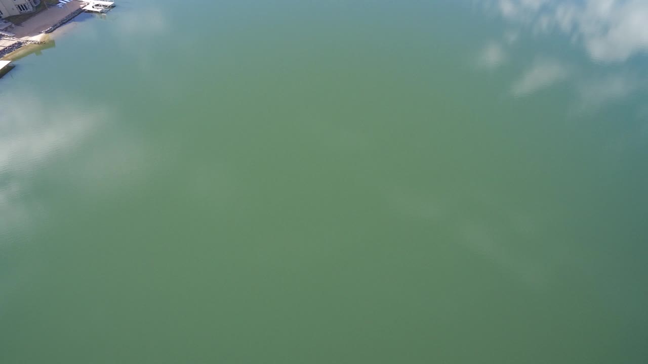 Aerial view over green-blue water with a small dock edge at the top.