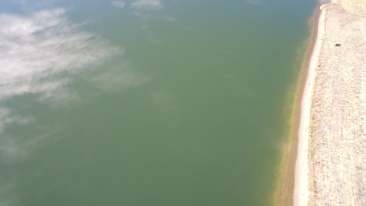 Aerial view of green water beside a pale narrow shoreline.