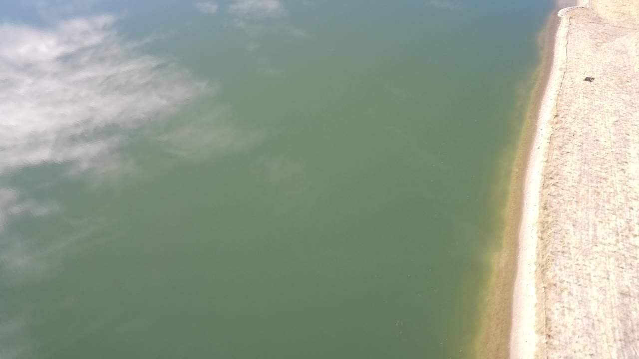 A later aerial frame in Westminster, Colorado keeps the green water dominant while the pale bank runs vertically along the right side with no visible people.