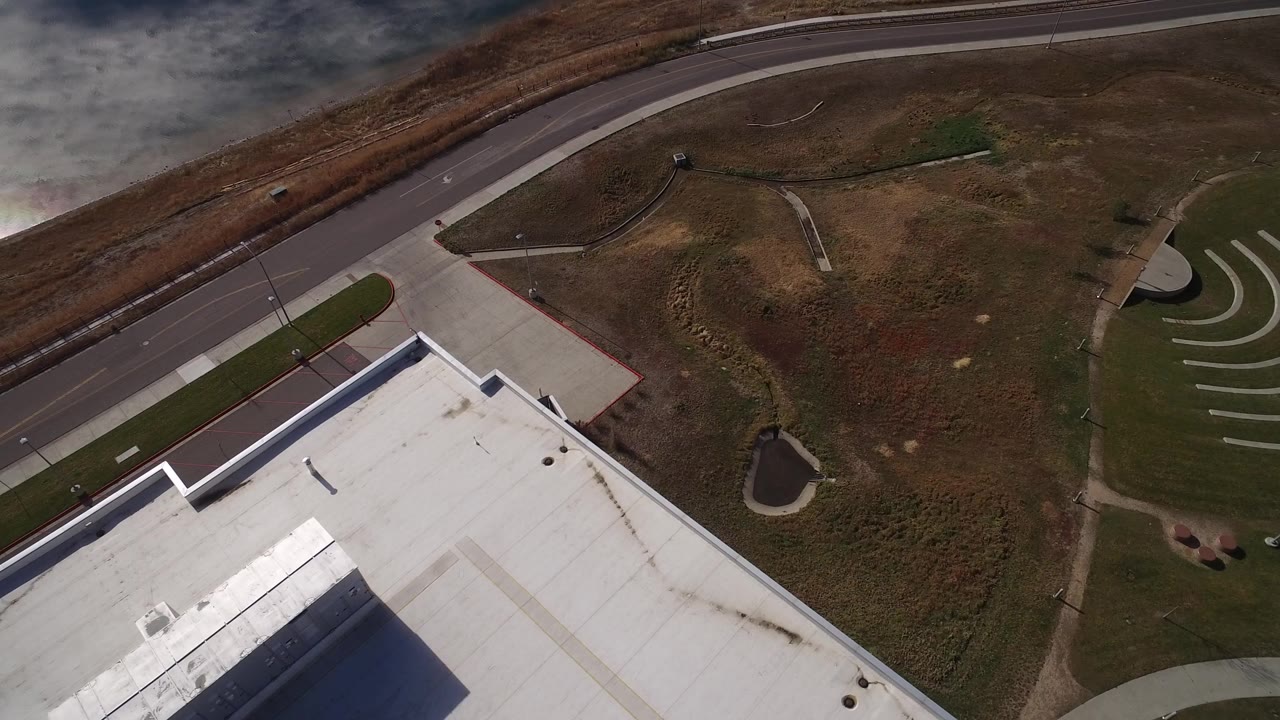 Aerial view of a white roof, curving road, grass, and small pond.