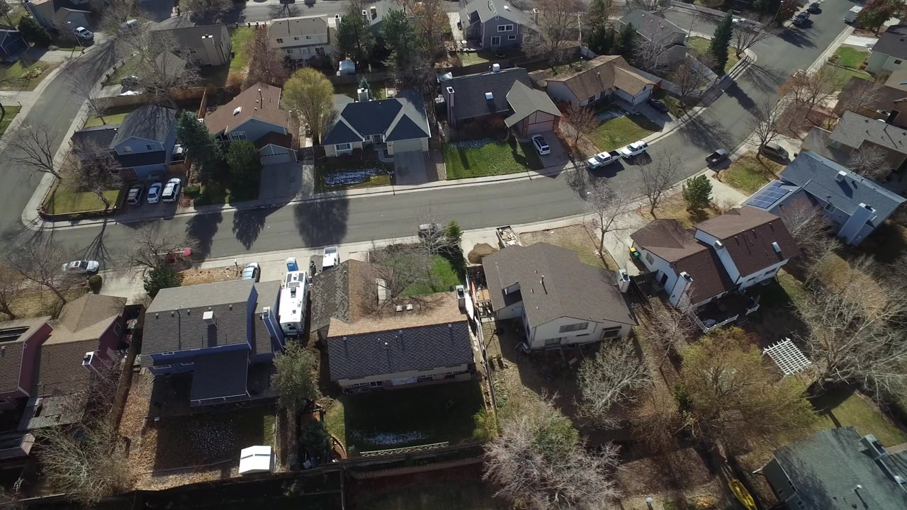 Overhead frame of Westminster, Colorado homes, fenced yards, parked cars, leafless trees, and a quiet residential street with no visible people.