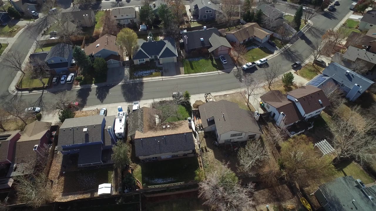 Aerial frame over Westminster, Colorado showing detached houses, backyards, driveway vehicles, winter-bare trees, and no visible people.