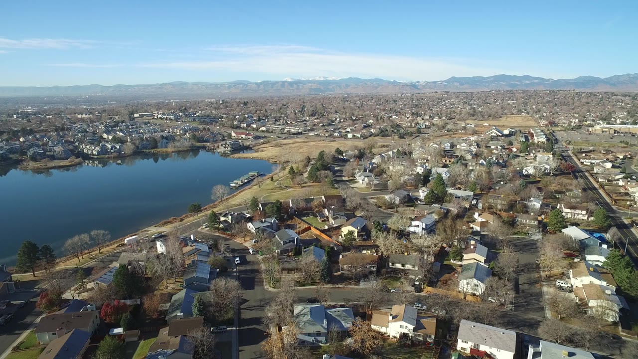 Aerial view of a lake beside suburban houses and distant mountains.