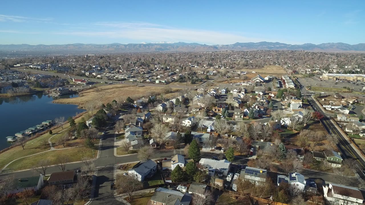 Aerial view of suburban homes, a lake, roads, open land, and distant hills.