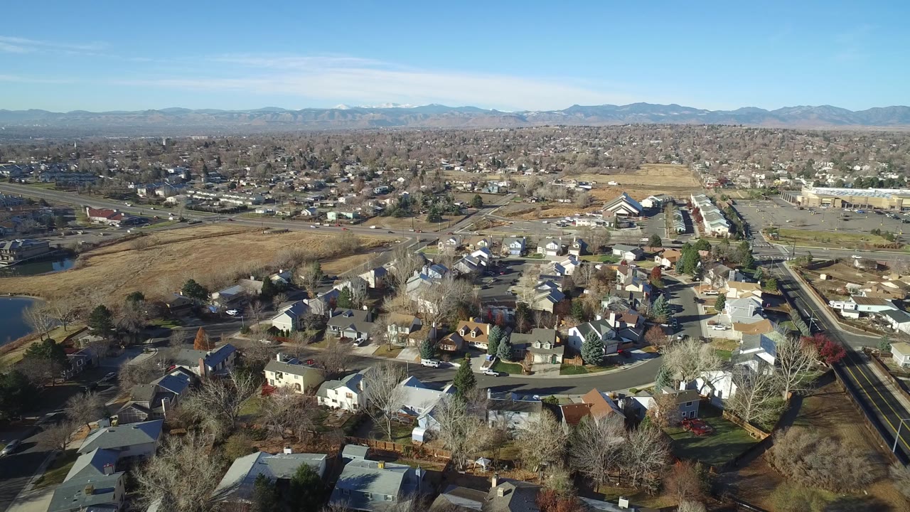 Aerial view of suburban houses, streets, open fields, and distant mountains.