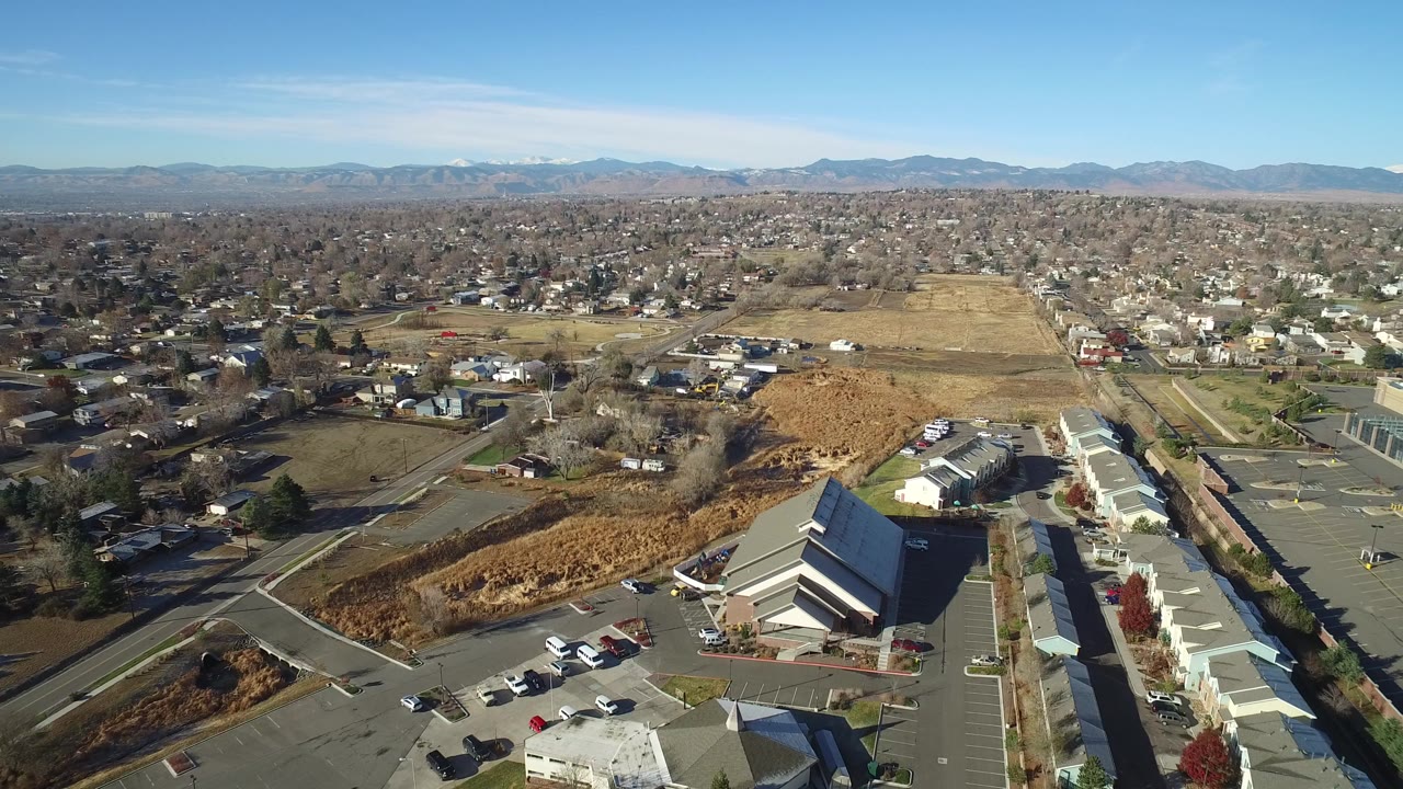 Aerial view over suburban roads, buildings, open fields, and distant mountains.