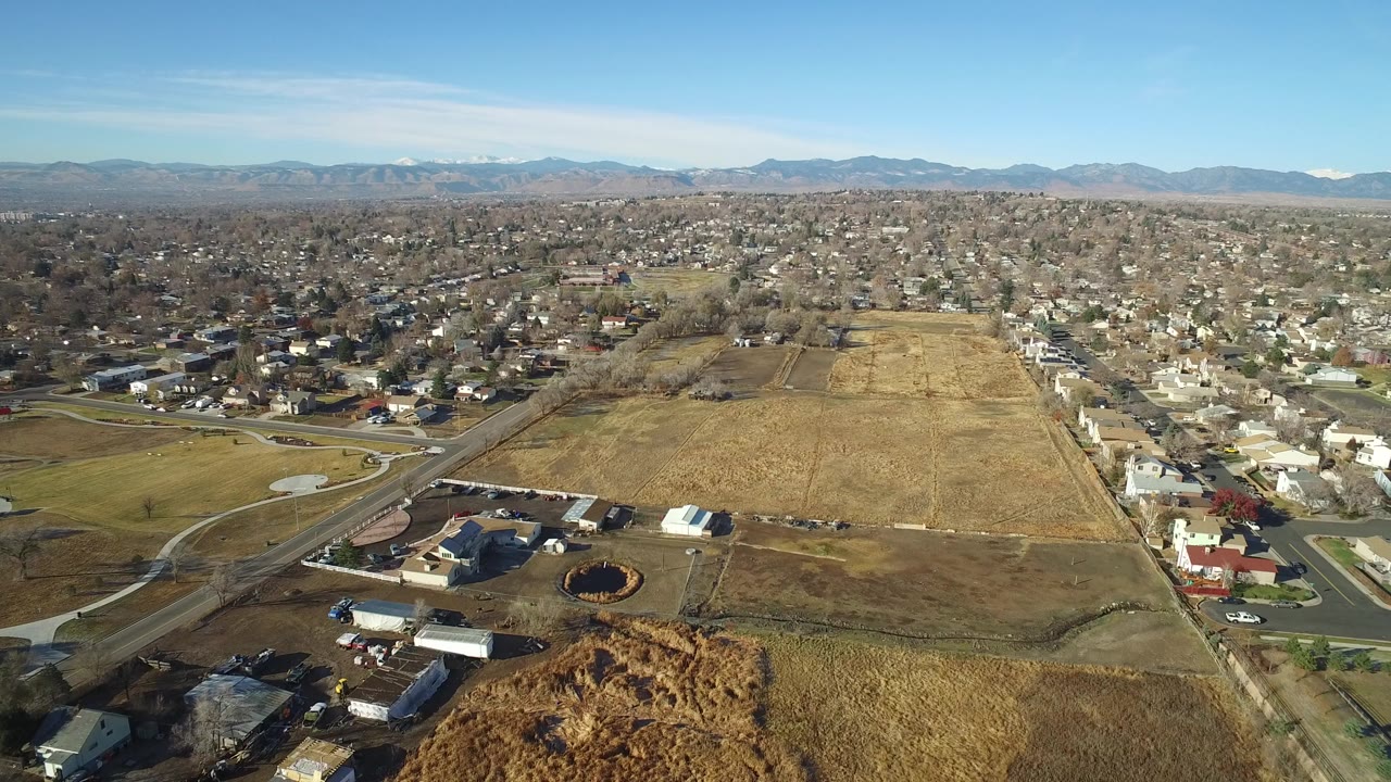 Aerial view of tan fields, suburban homes, roads, and distant mountains.