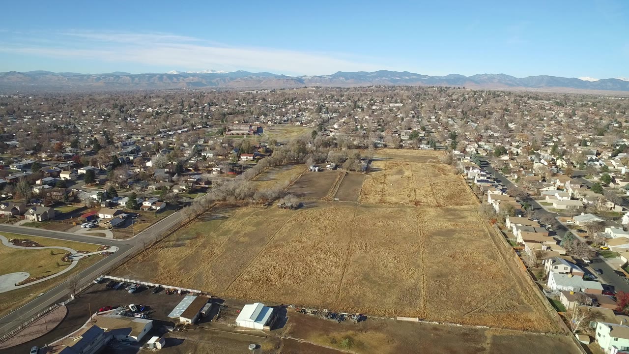 Aerial view over dry fields, homes, streets, and distant mountains.