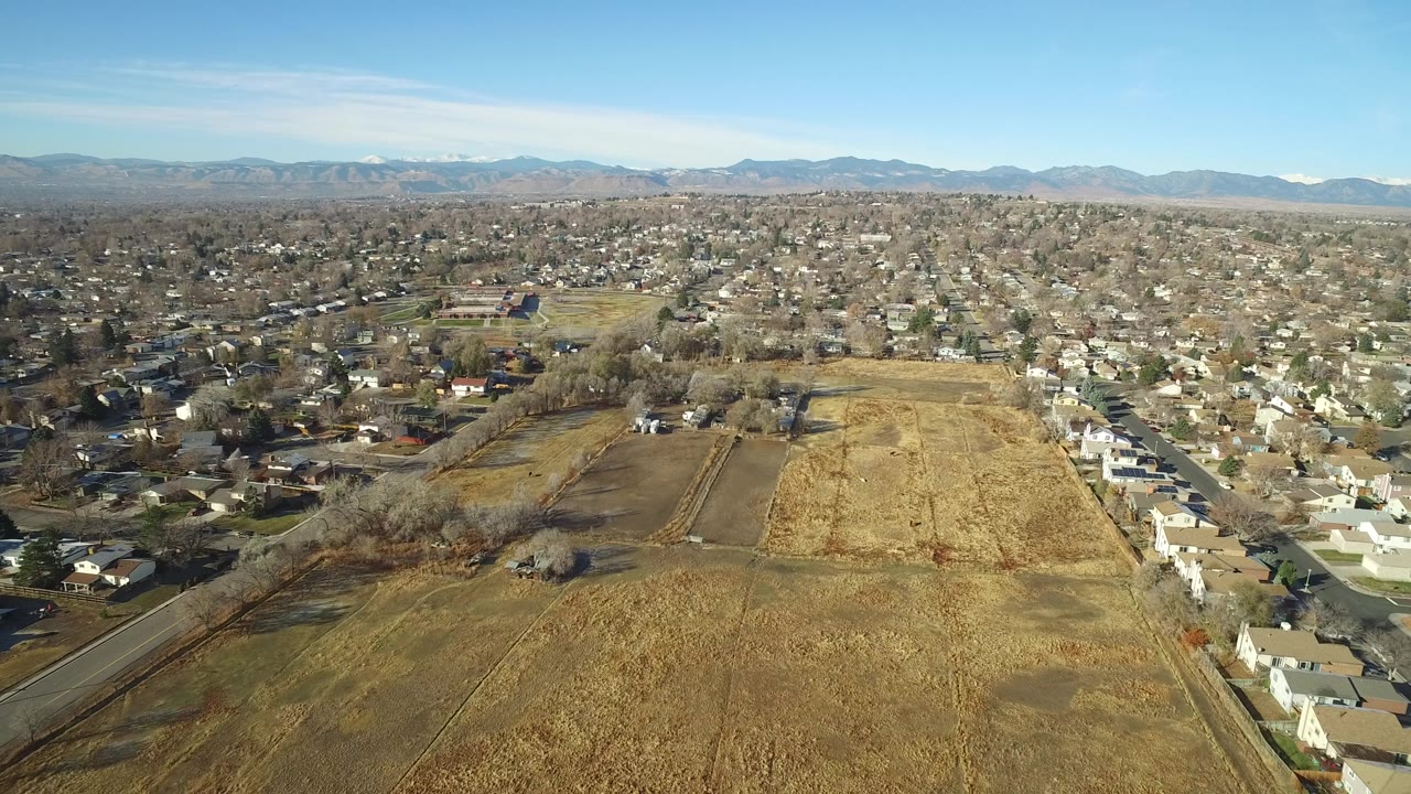 Aerial view over a dry field beside suburban streets and houses.