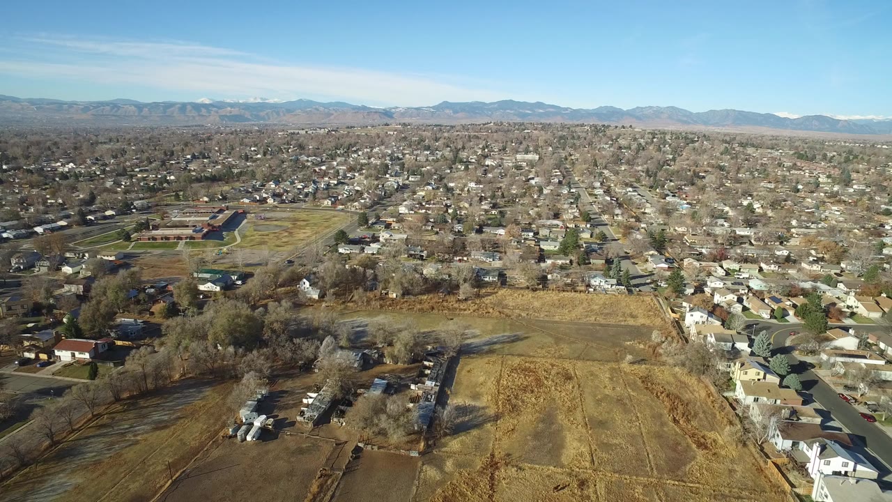 Aerial view over dry fields, homes, and distant mountains.