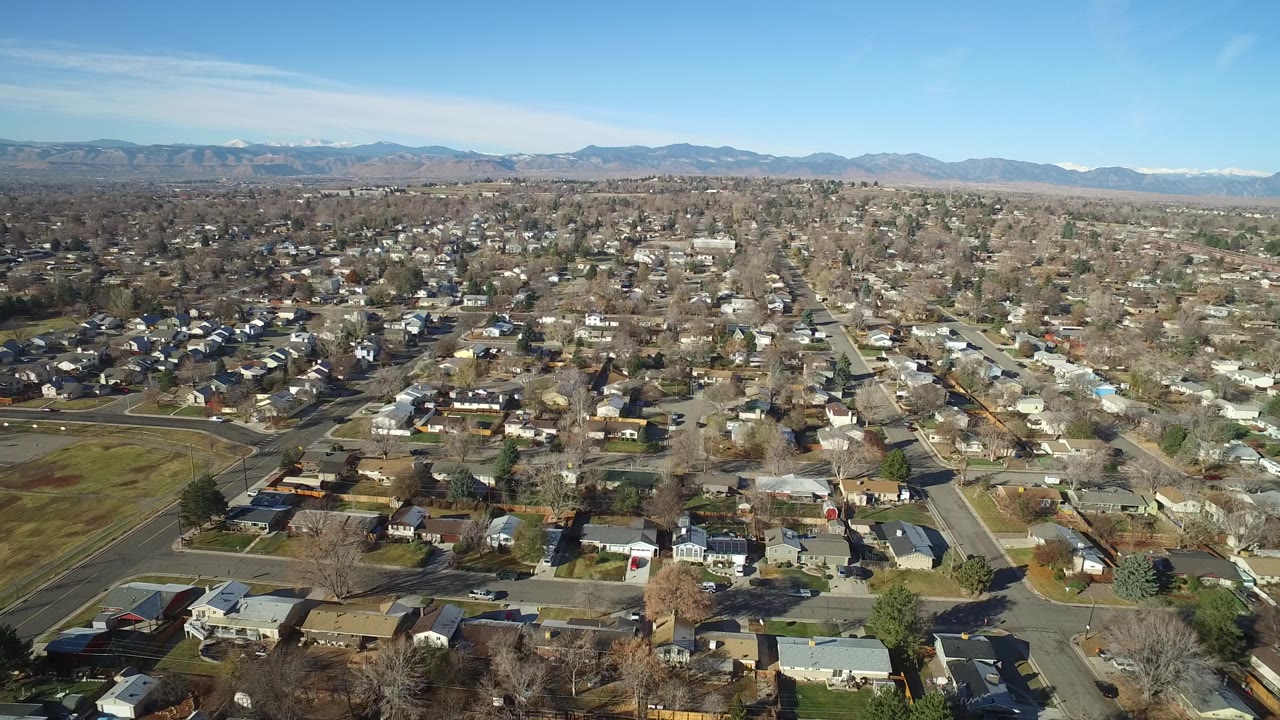 High drone-style view across Westminster, Colorado residential blocks, a small green open area, intersecting roads, and distant foothills, with no visible people.