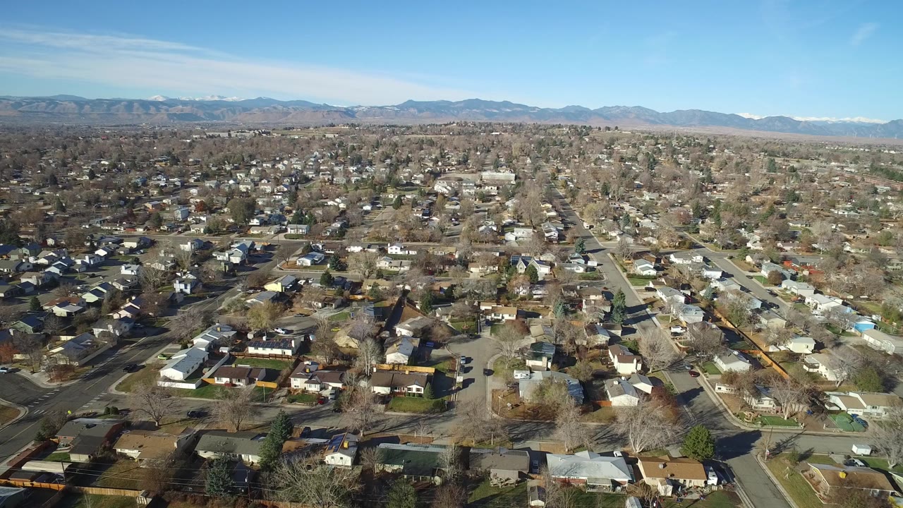 A high aerial frame shows Westminster, Colorado rooftops and intersecting neighborhood streets beneath a clear sky, with no visible people.