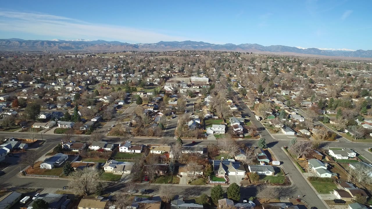 Wide aerial view of suburban homes, streets, trees, and distant mountains.