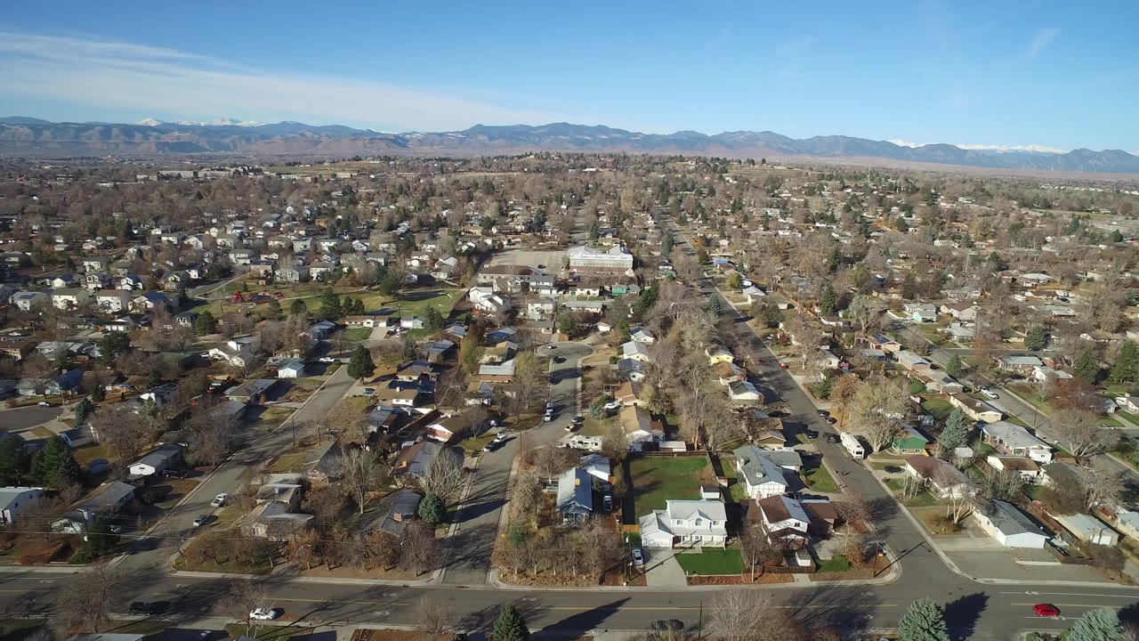 Wide aerial view over suburban homes and streets with mountains beyond.