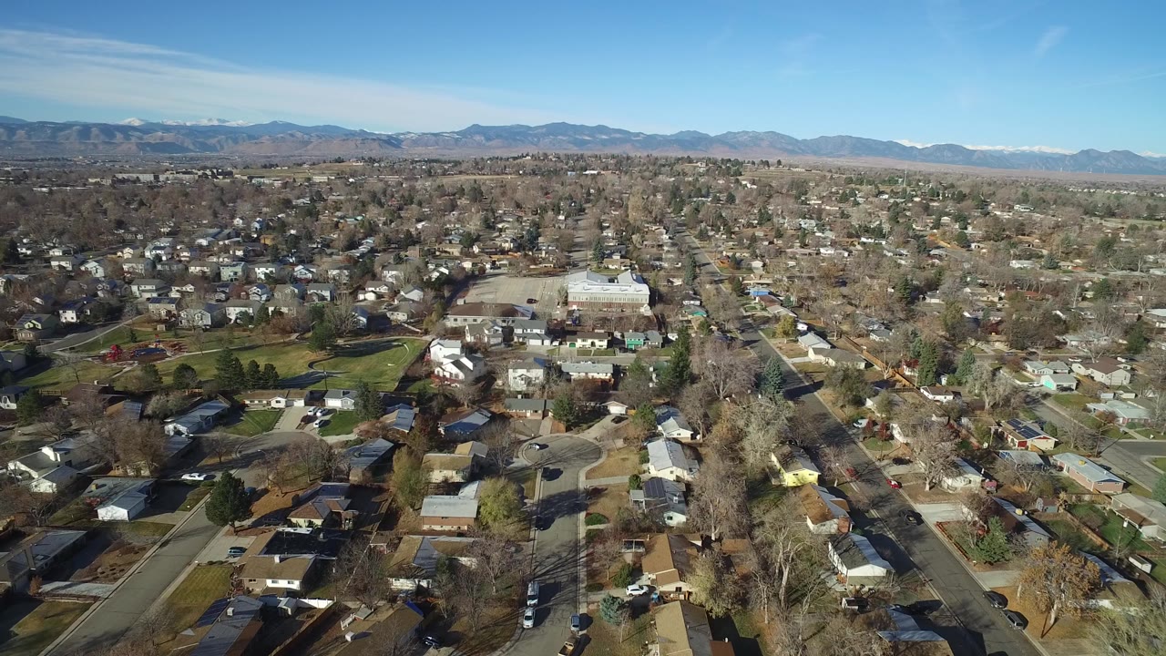 Suburban rooftops and streets stretch toward a mountain range in bright sun.