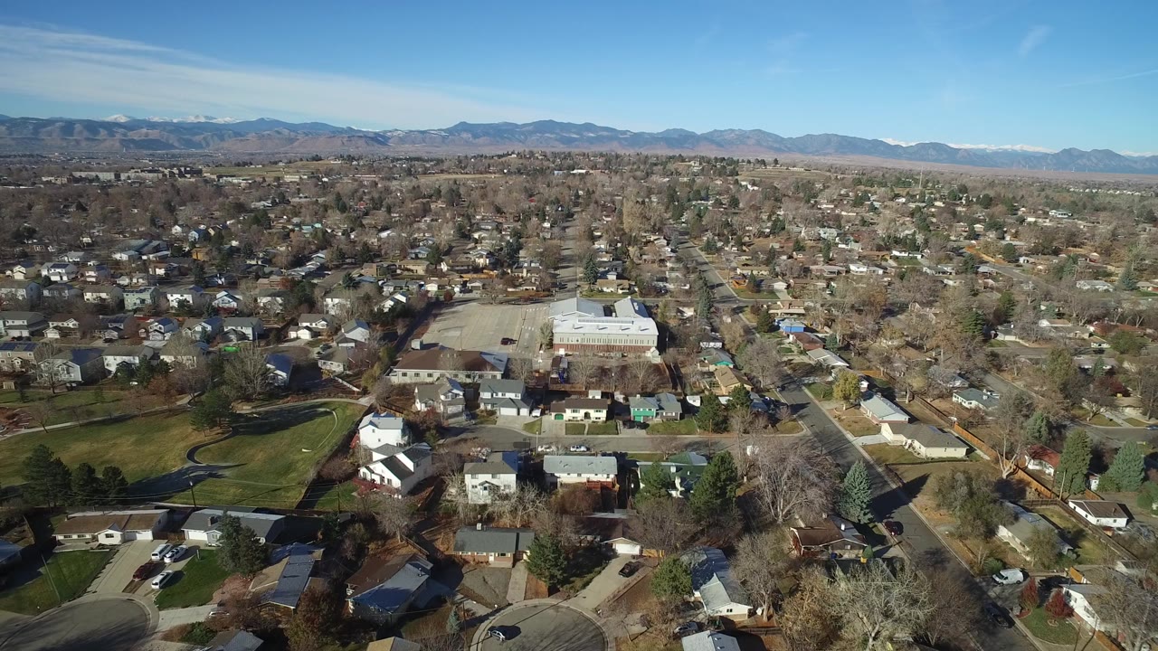 Suburban aerial with homes, lawns, roads, and a mountain backdrop.