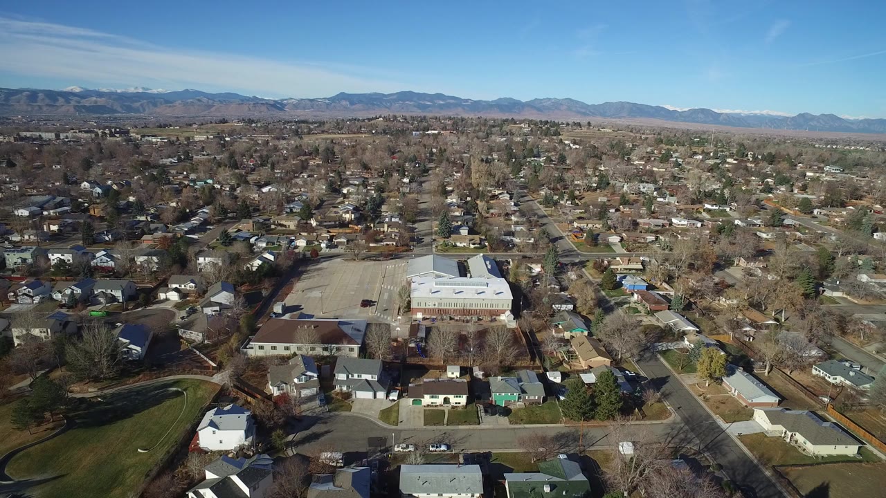 Aerial view over suburban streets and homes with mountains in the distance.