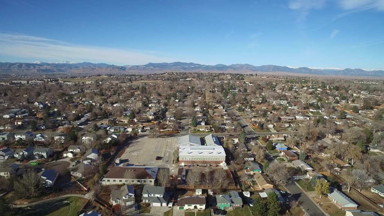 High aerial view of suburban streets, homes, trees, and distant mountains.