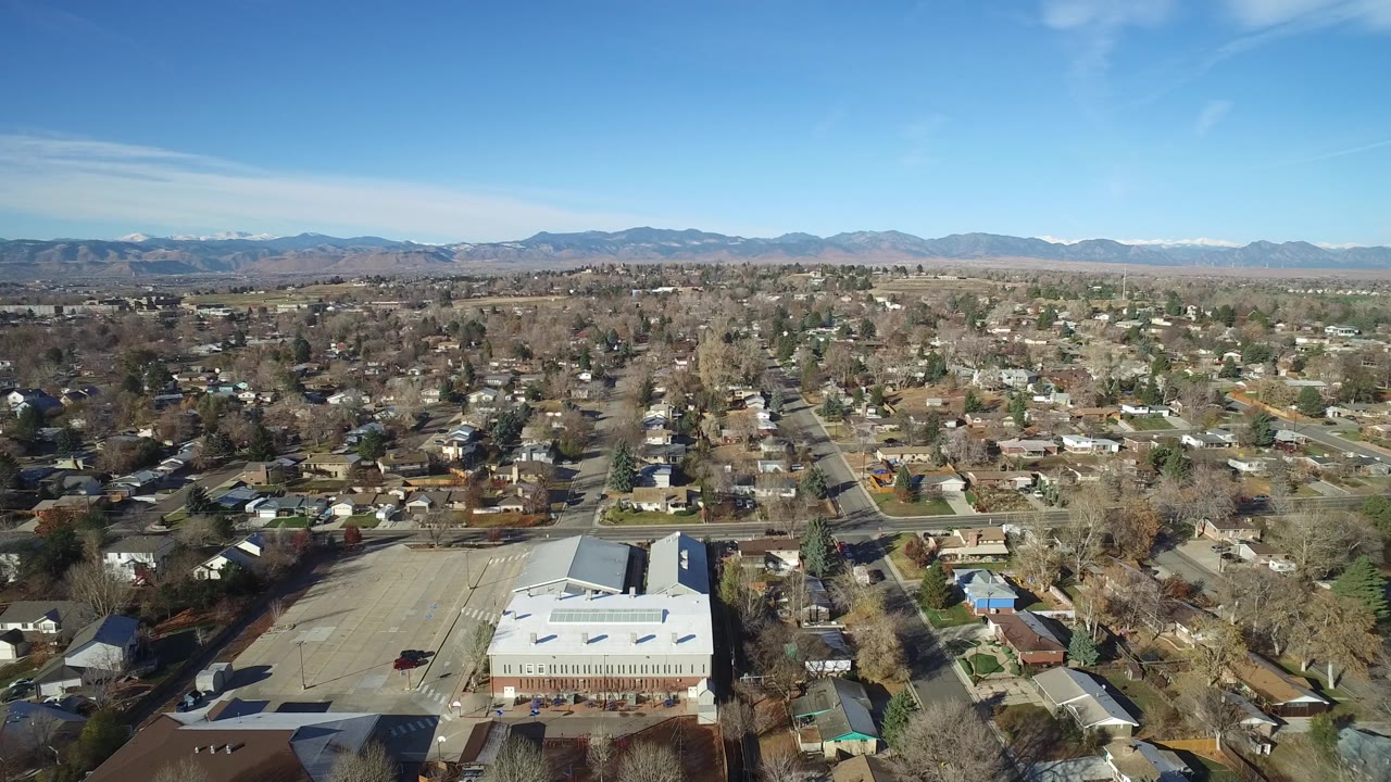 High aerial over houses and roads with mountains under a clear blue sky.