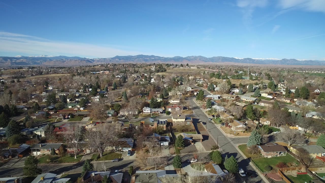 Aerial view over suburban homes and tree-lined streets with mountains in the distance.
