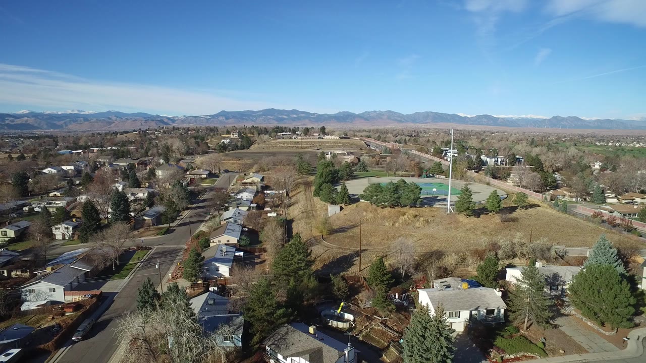 Aerial view over homes, trees, roads, tennis courts, and distant mountains.