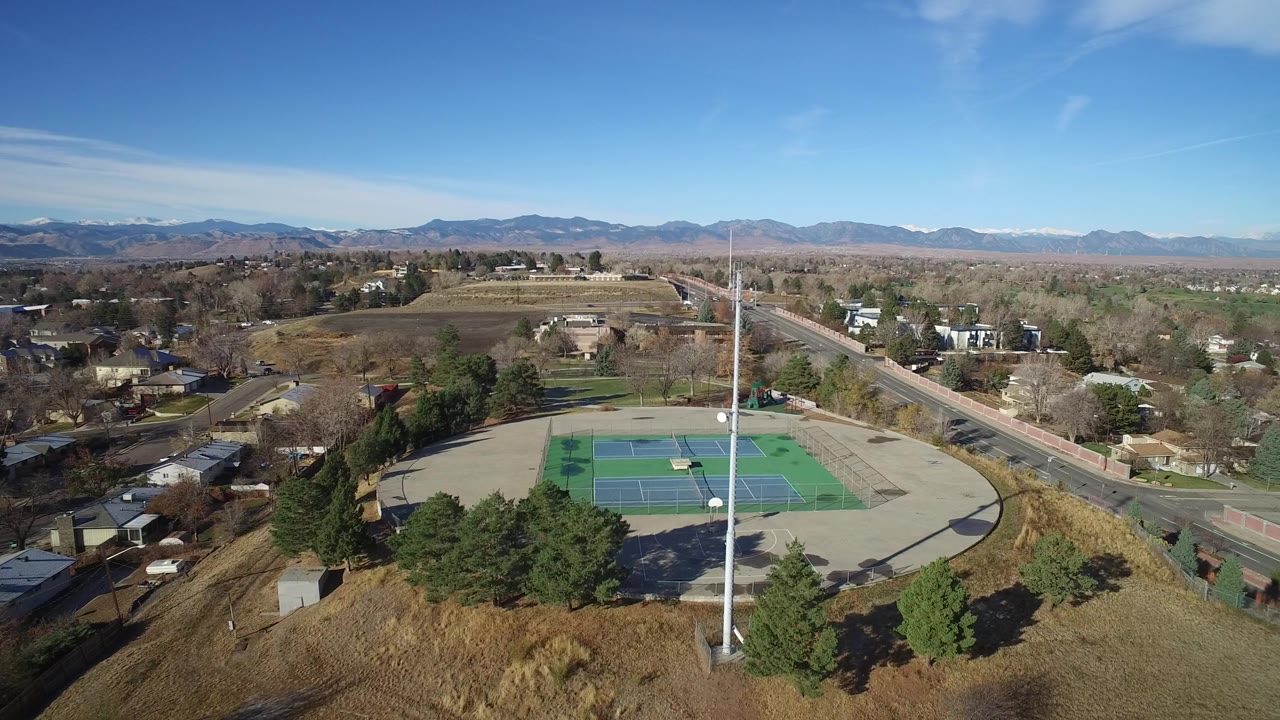 Aerial view of tennis courts beside suburban streets and distant mountains.