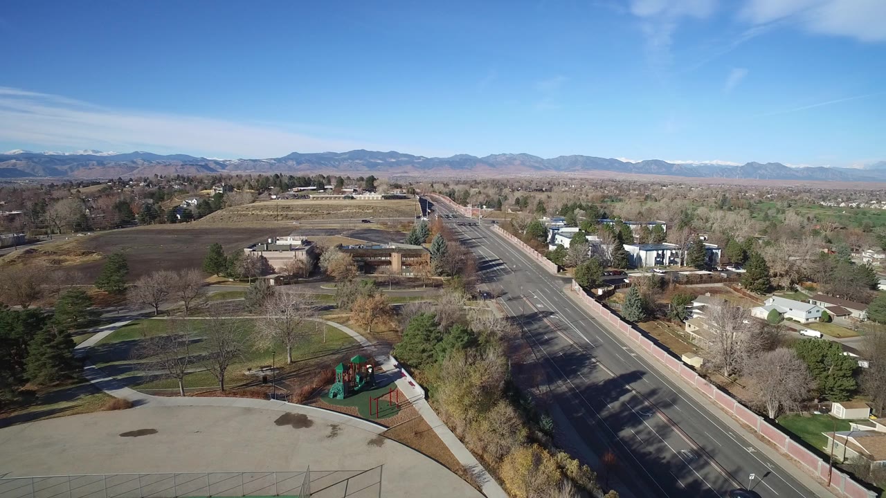 Aerial view of suburban road, playground, houses, trees, and distant mountains.