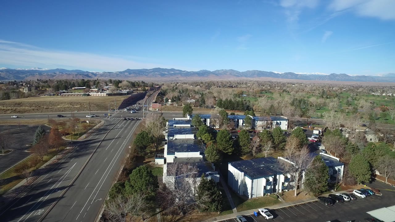 Aerial view of low buildings, parking lots, roads, trees, and distant mountains.