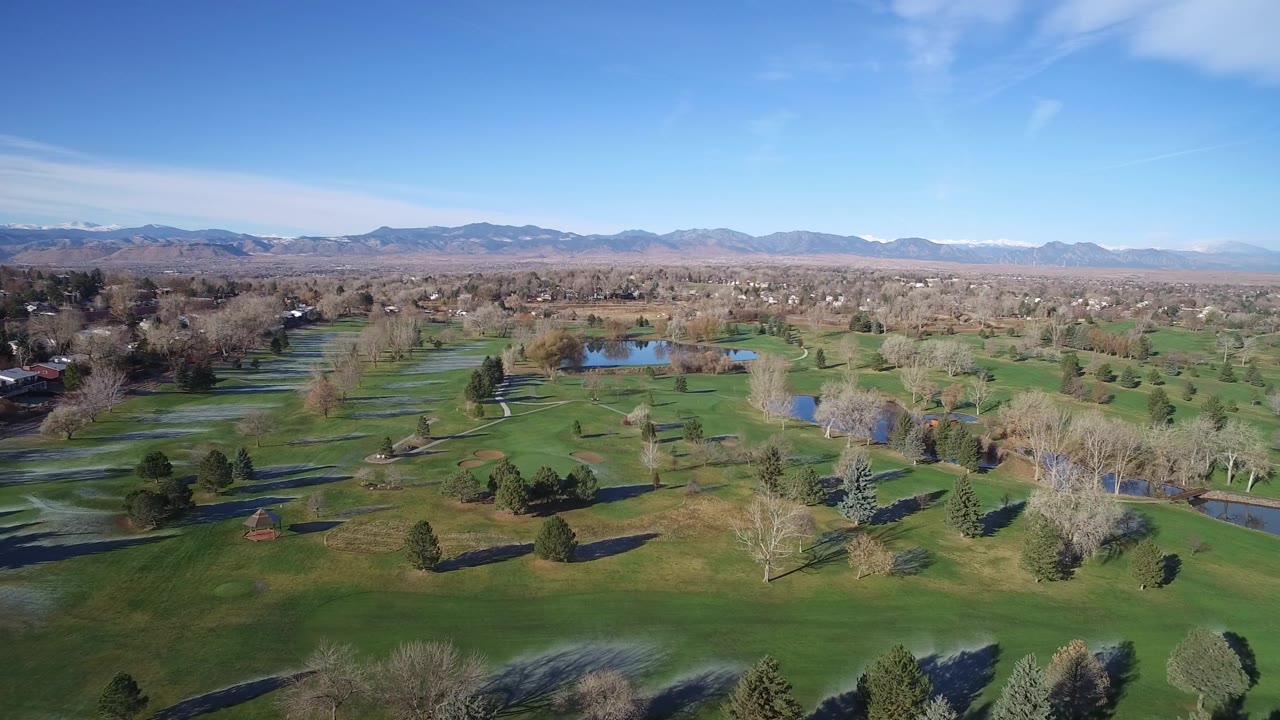 Drone-height landscape with water, trees, lawns, houses, and mountains