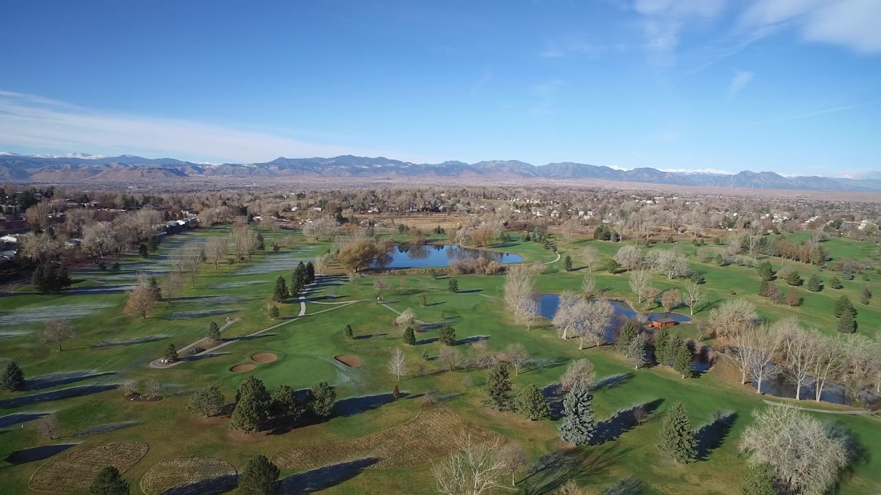 Green course terrain with ponds, tree lines, paths, and a mountain horizon.