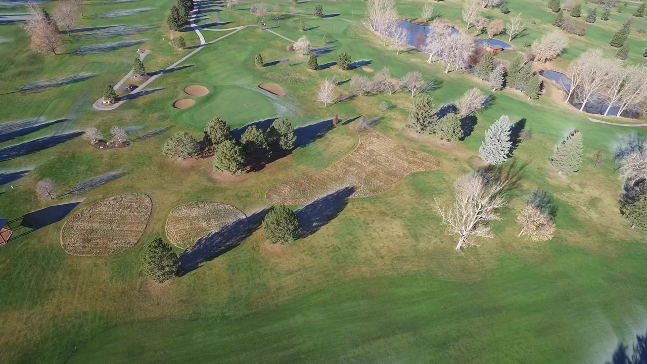 Aerial view of green parkland with sand bunkers, paths, ponds, and trees.