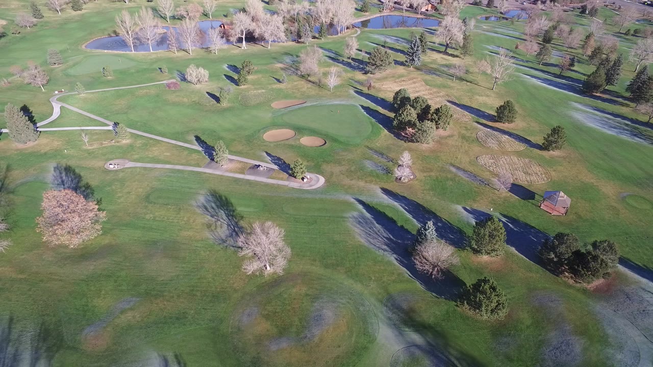 Aerial view of an empty golf course with fairways, paths, trees, sand traps, and a small lake.
