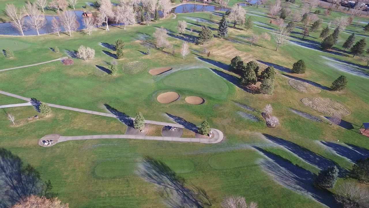 Aerial view of green fairways, cart paths, ponds, trees, and sand bunkers.