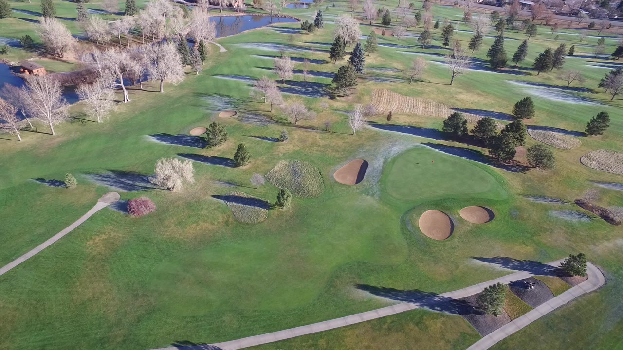 Aerial view of green fairways, sand bunkers, cart paths, trees, and water.