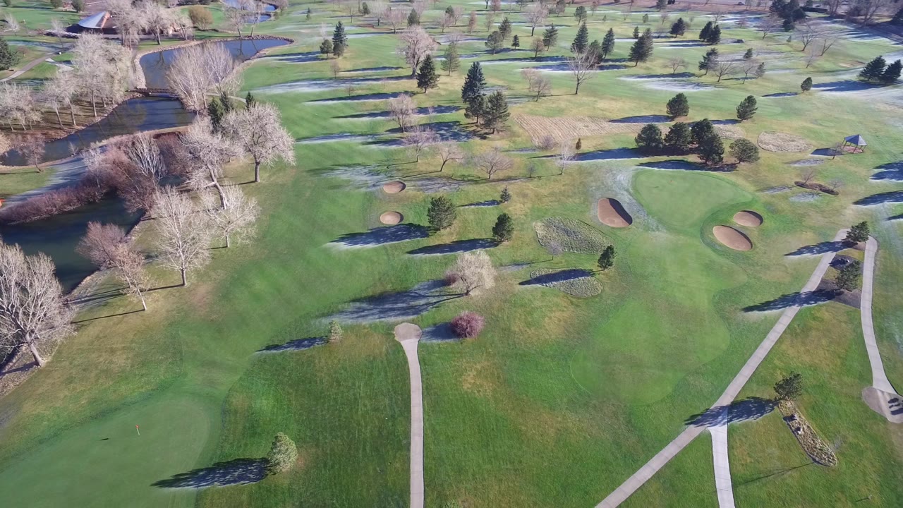 Aerial frame over Westminster, Colorado showing a central green area, two sand bunkers, a winding path network, ponds, trees, and no visible people.