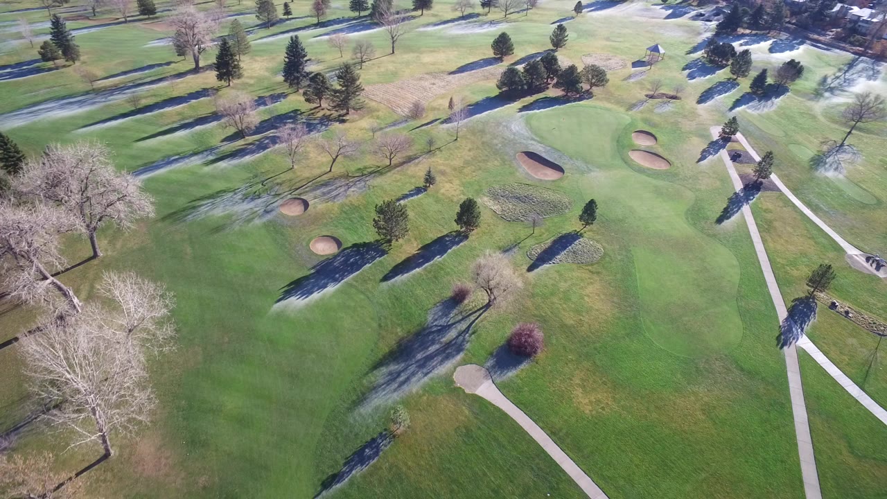 Aerial view of a golf course with greens, bunkers, trees, and cart paths.