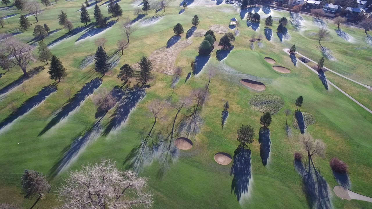 Aerial view of green fairways, sand bunkers, trees, and long shadows.