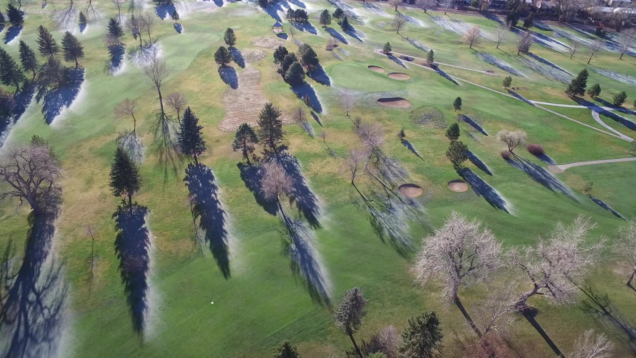 Aerial view of green lawns, trees, paths, sand bunkers, and sprinkler mist.