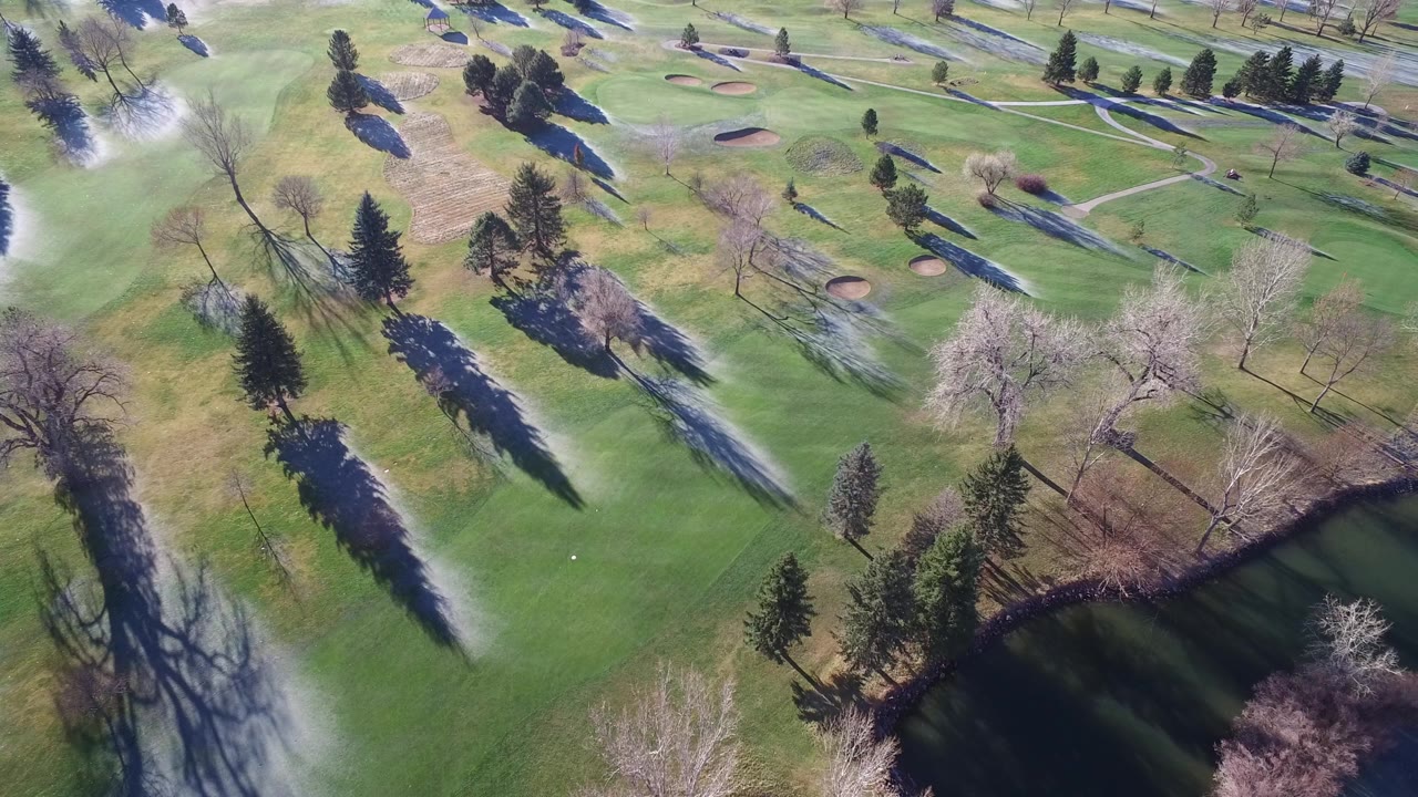 High-angle view of trees, fairways, sand traps, paths, and a pond corner.