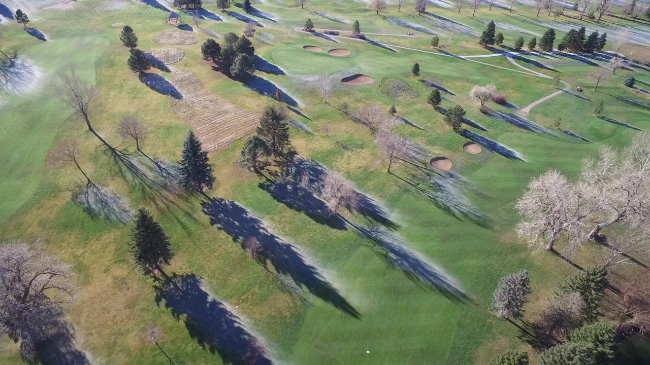 High aerial frame in Westminster, Colorado with curving paths, pale sand bunkers, mixed trees, green grass, and narrow snow streaks, with no visible people.
