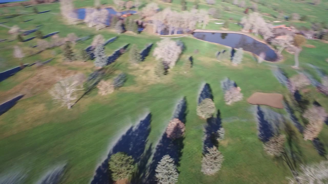 Elevated aerial view in Westminster, Colorado with fairways crossing the frame, a pond near the top, clustered trees, one visible sand bunker, and no visible people.