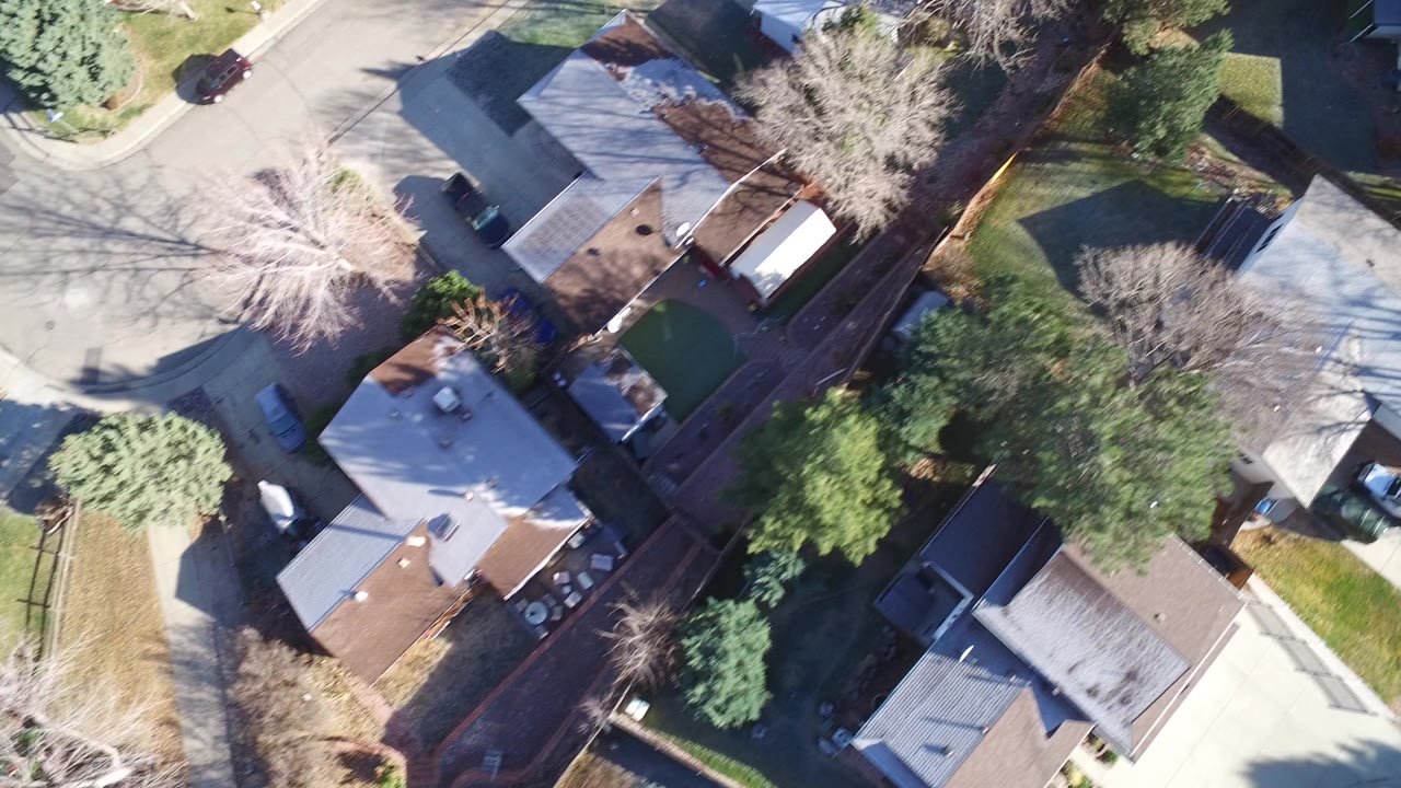 Overhead view of houses, streets, trees, and parked cars.